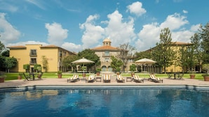 Zona de piscina con sillas de descanso y sombrillas, rodeada de edificios de estilo mediterráneo.