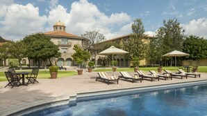 A pool area with lounge chairs and umbrellas, surrounded by a courtyard with trees and a building with a dome.