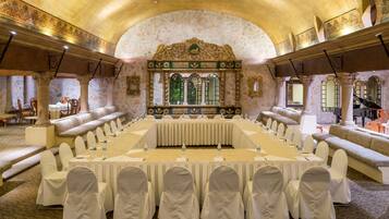 Un salón de conferencias con una larga mesa, sillas blancas y un decorado ornamental.