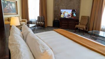 Ein Hotelzimmer mit einem großen Bett, einem Schreibtisch, einem Sessel, einem Fernseher und einem Bild an der Wand.