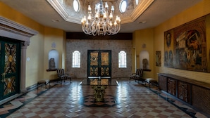 Un gran salón con suelo de cuadros, una araña central y arte clásico en las paredes.