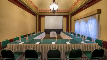 Un salón de conferencias con una larga mesa, sillas, una pantalla de proyector y una araña.