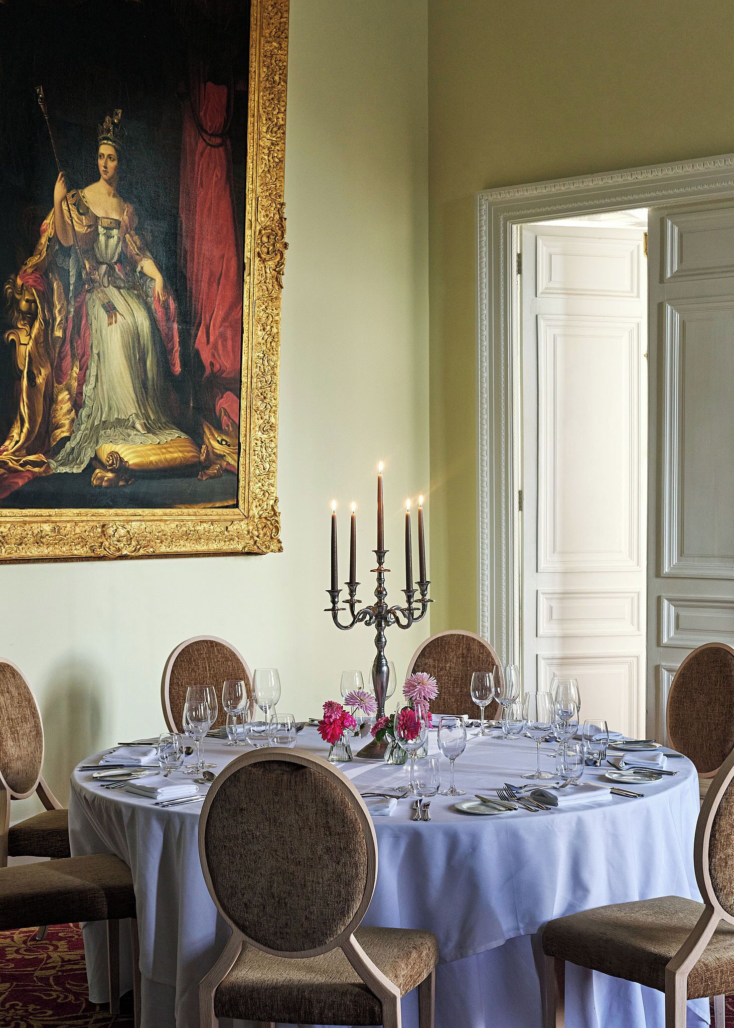 Een elegante eetzaal met een gedekte tafel voor zes personen, een kandelaar en een klassiek schilderij aan de muur.