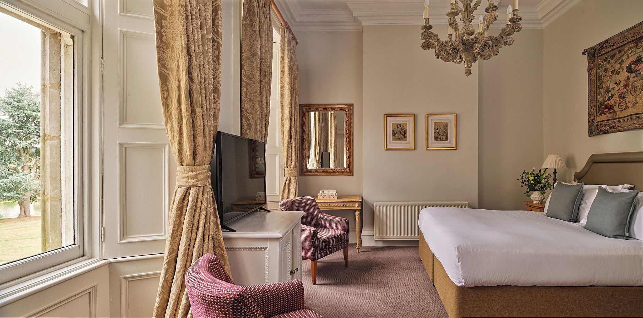 A hotel room with a bed, a television, a chair, a table, and a large window.
