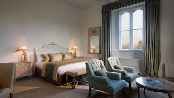 A bedroom with a bed, two armchairs, a nightstand, a table, and a window with curtains.