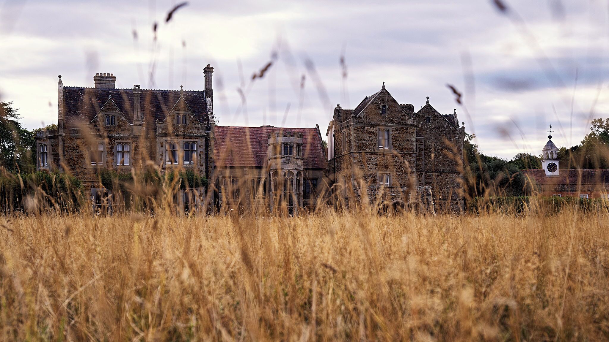 A historic building with multiple towers and a clock tower, surrounded by tall grass.
