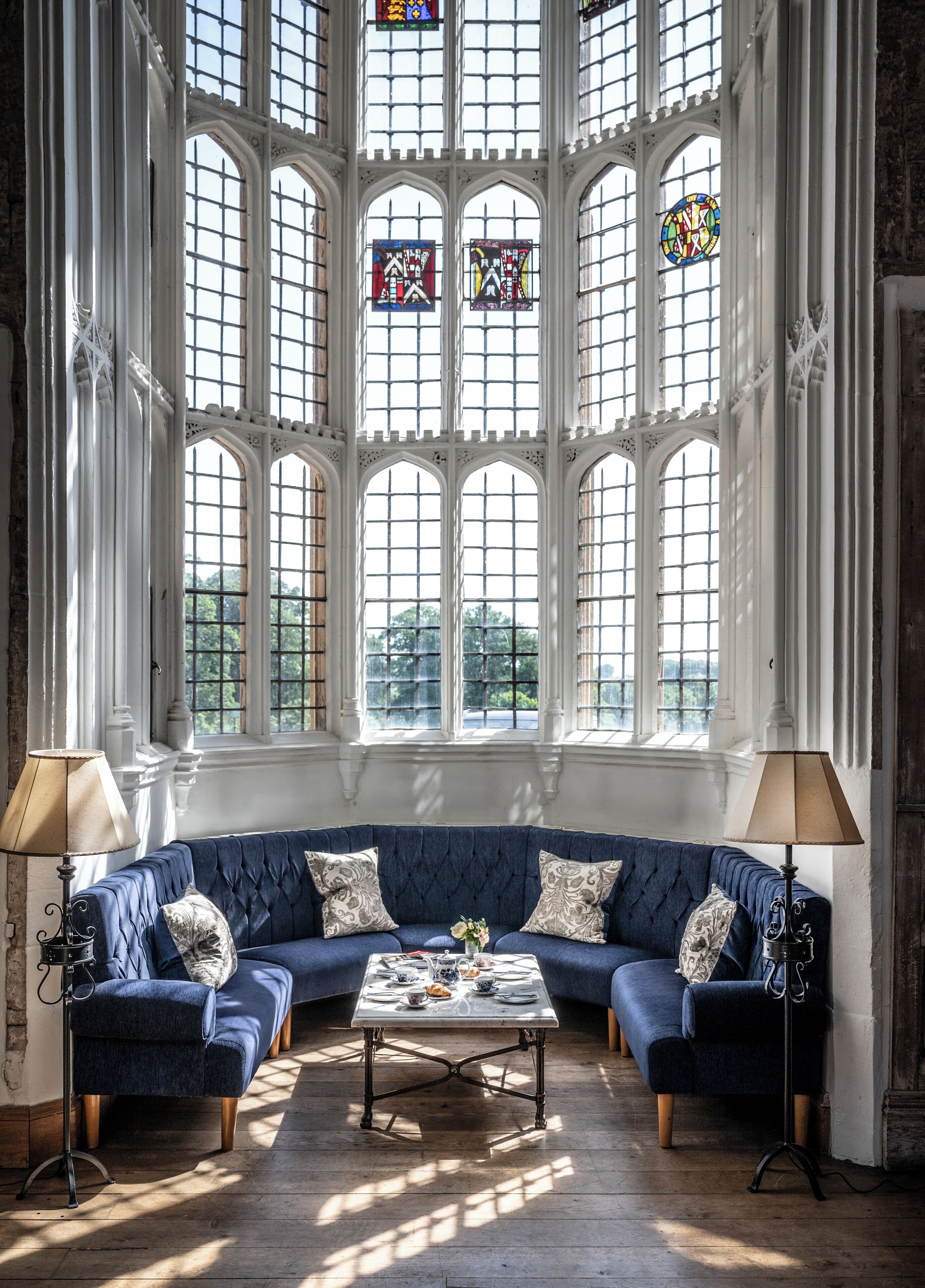 A room with a blue upholstered sofa, a coffee table, and a large window with stained glass.
