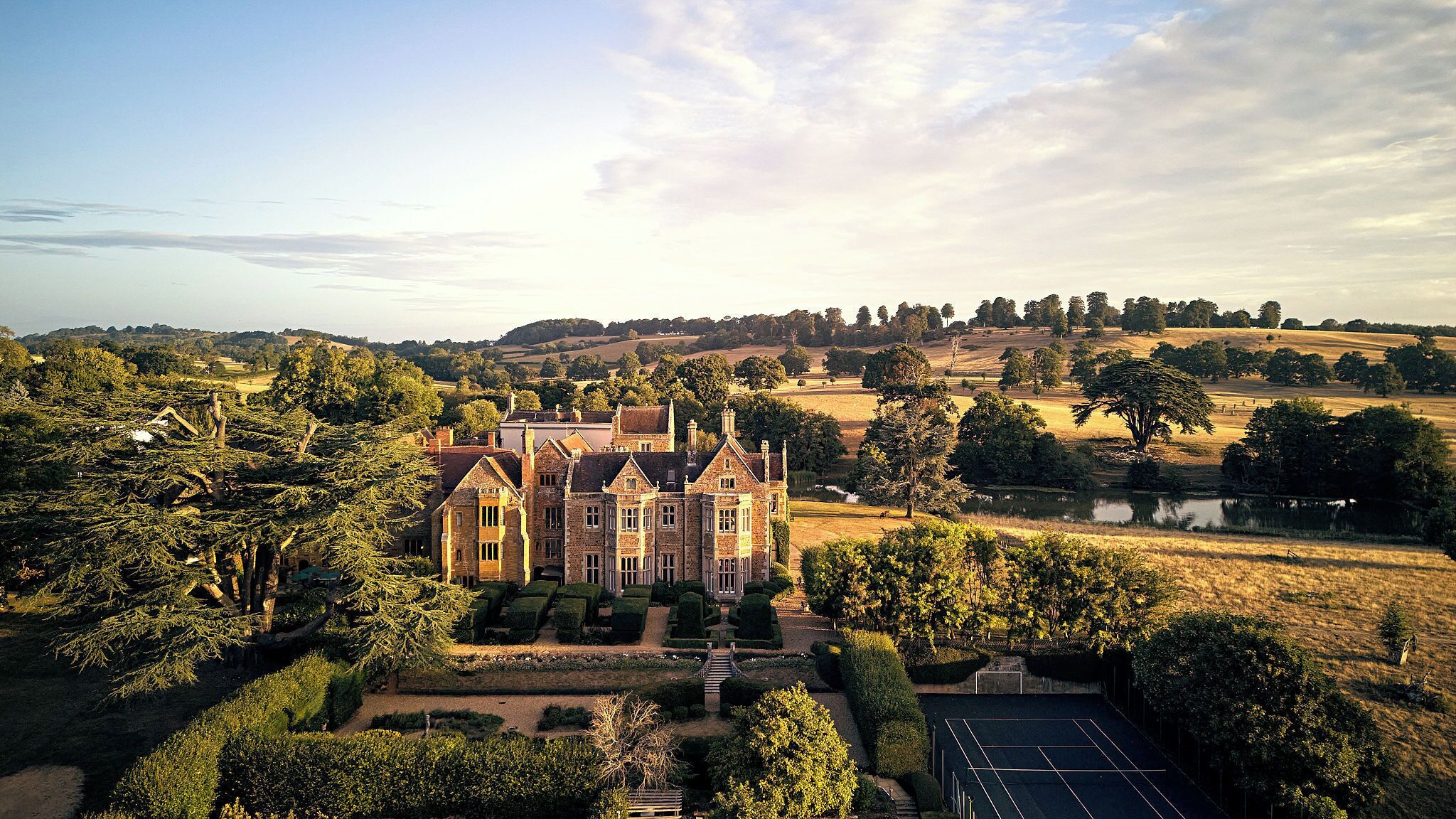 A large, historic building with a formal garden and tennis court.