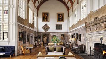 A spacious room with high ceilings, wooden beams, and a fireplace. There are multiple seating areas with tables and chairs.