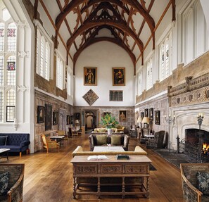 A spacious room with high ceilings, wooden beams, and a fireplace. There are multiple seating areas with tables and chairs.