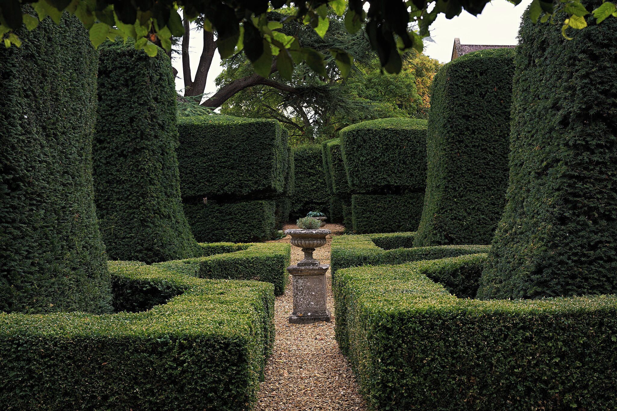 A formal garden with neatly trimmed hedges and a central stone structure.