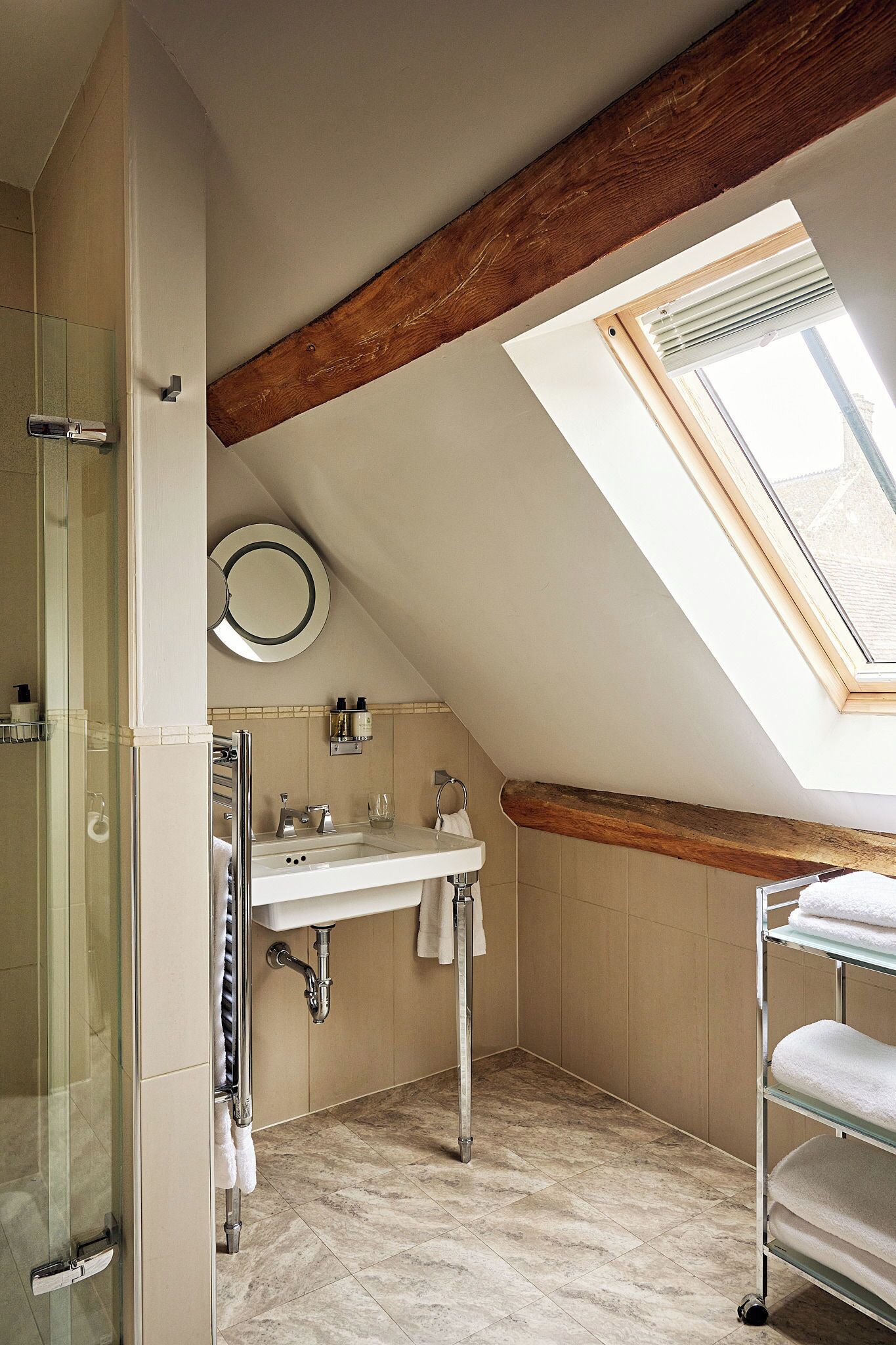 A bathroom with a skylight, a glass shower enclosure, a sink, and a towel rack.