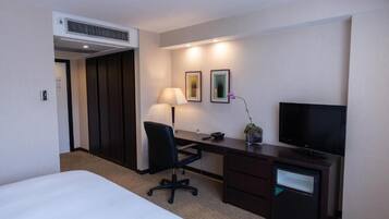 A hotel room with a bed, a desk with a chair, a television, a lamp, and two framed pictures on the wall.