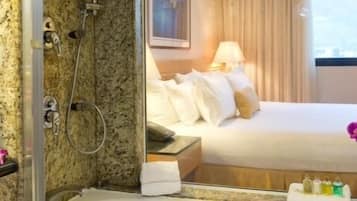 A hotel room with a bed, a bathroom with a shower, and a window with curtains.