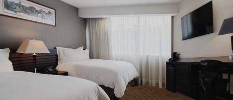 A hotel room with two beds, a desk, a chair, a TV, and a window with curtains.