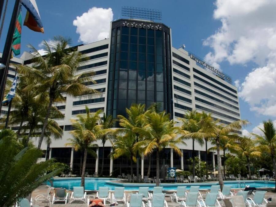 A hotel with a pool area, palm trees, and a modern building facade.