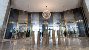 Un hall d’entrée moderne avec un lustre central, des murs en verre et un sol en marbre.