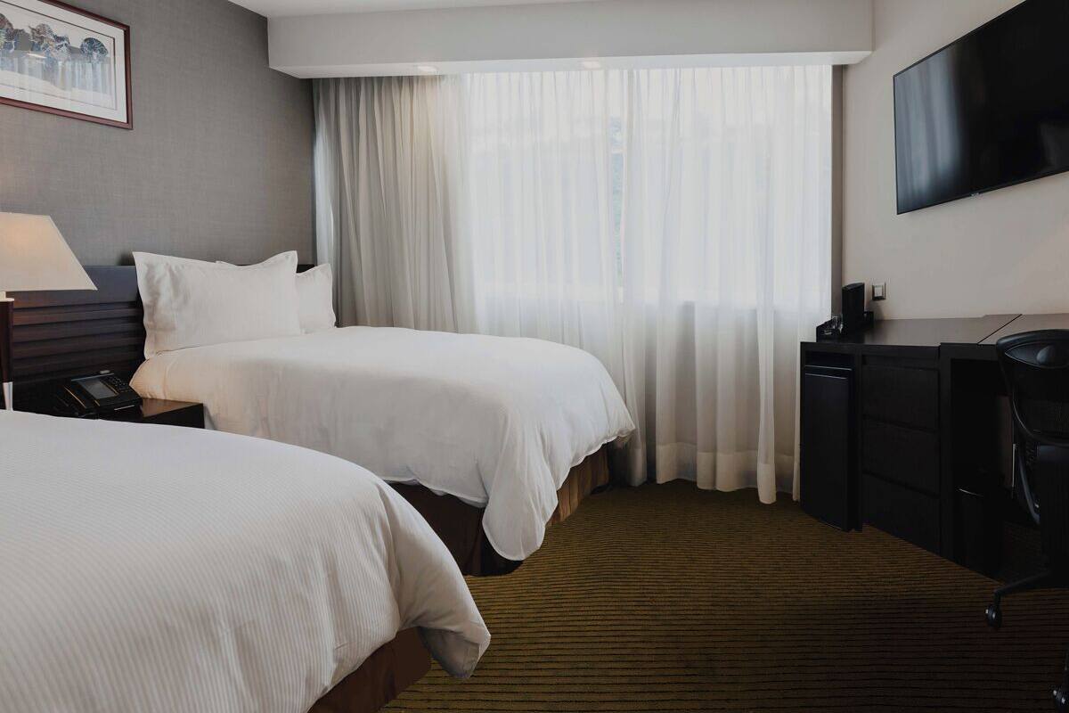 Une chambre d’hôtel avec deux lits, un bureau, une télévision et une fenêtre avec des rideaux.