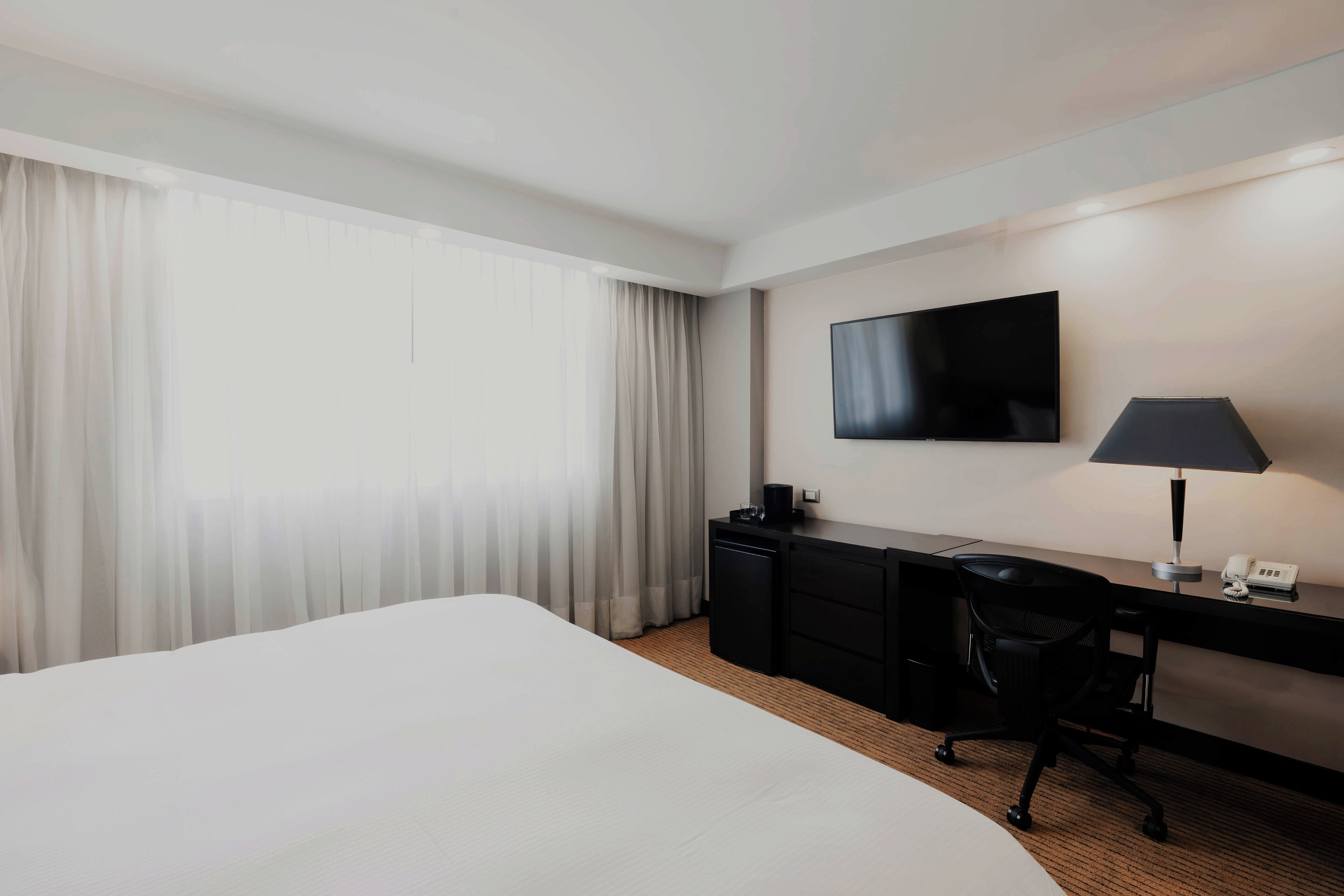 Habitación de hotel con una cama grande, un escritorio con lámpara, un televisor de pantalla plana y un teléfono.