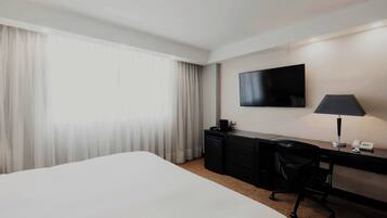Habitación de hotel con una cama grande, un escritorio con lámpara, un televisor de pantalla plana y un teléfono.