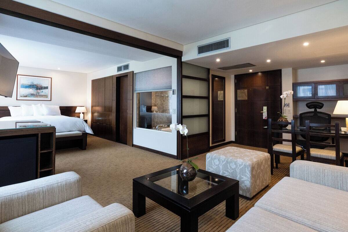 Une chambre d’hôtel comprenant un lit, un bureau, une chaise, un canapé et une petite table sur laquelle se trouve un vase.