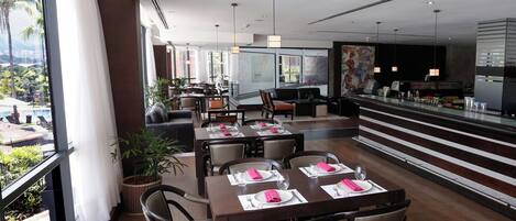 A modern dining area with tables set for four, large windows, and a view of the outdoors.