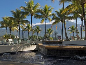 A pool area with lounge chairs, palm trees, and flags.
