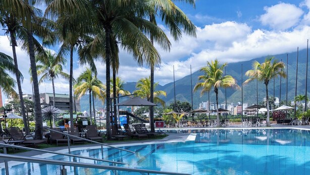 Une piscine entourée de chaises longues et de parasols, avec des palmiers et des montagnes en toile de fond.