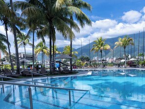 A swimming pool with lounge chairs and umbrellas, surrounded by palm trees and mountains in the background. - Eurobuilding Hotel & Suites Caracas (Caracas)