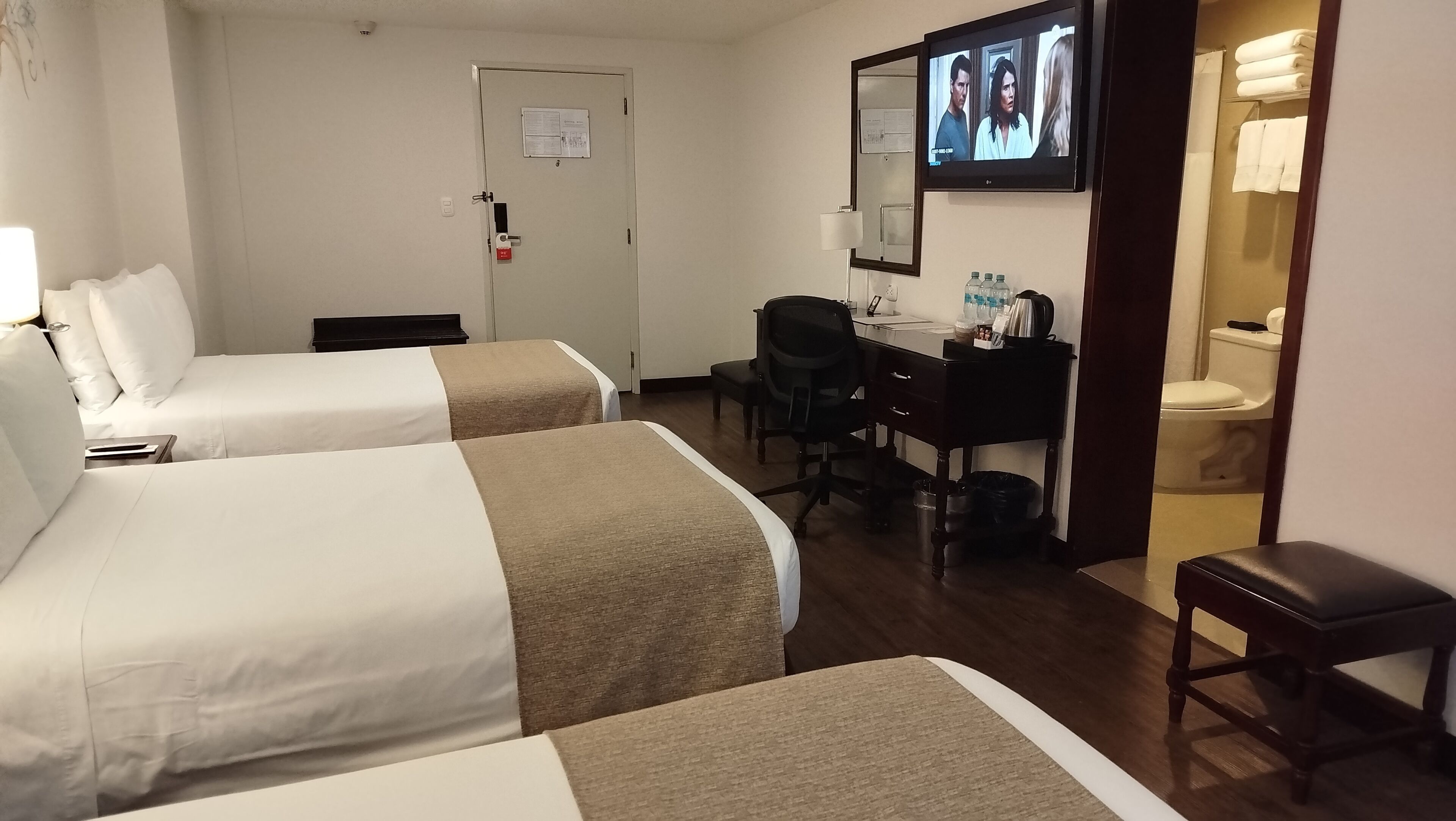 A hotel room with two beds, a desk, a chair, a television, and a bathroom.
