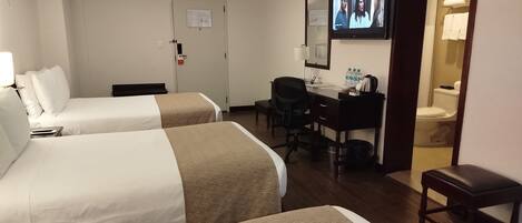 A hotel room with two beds, a desk, a chair, a television, and a bathroom.