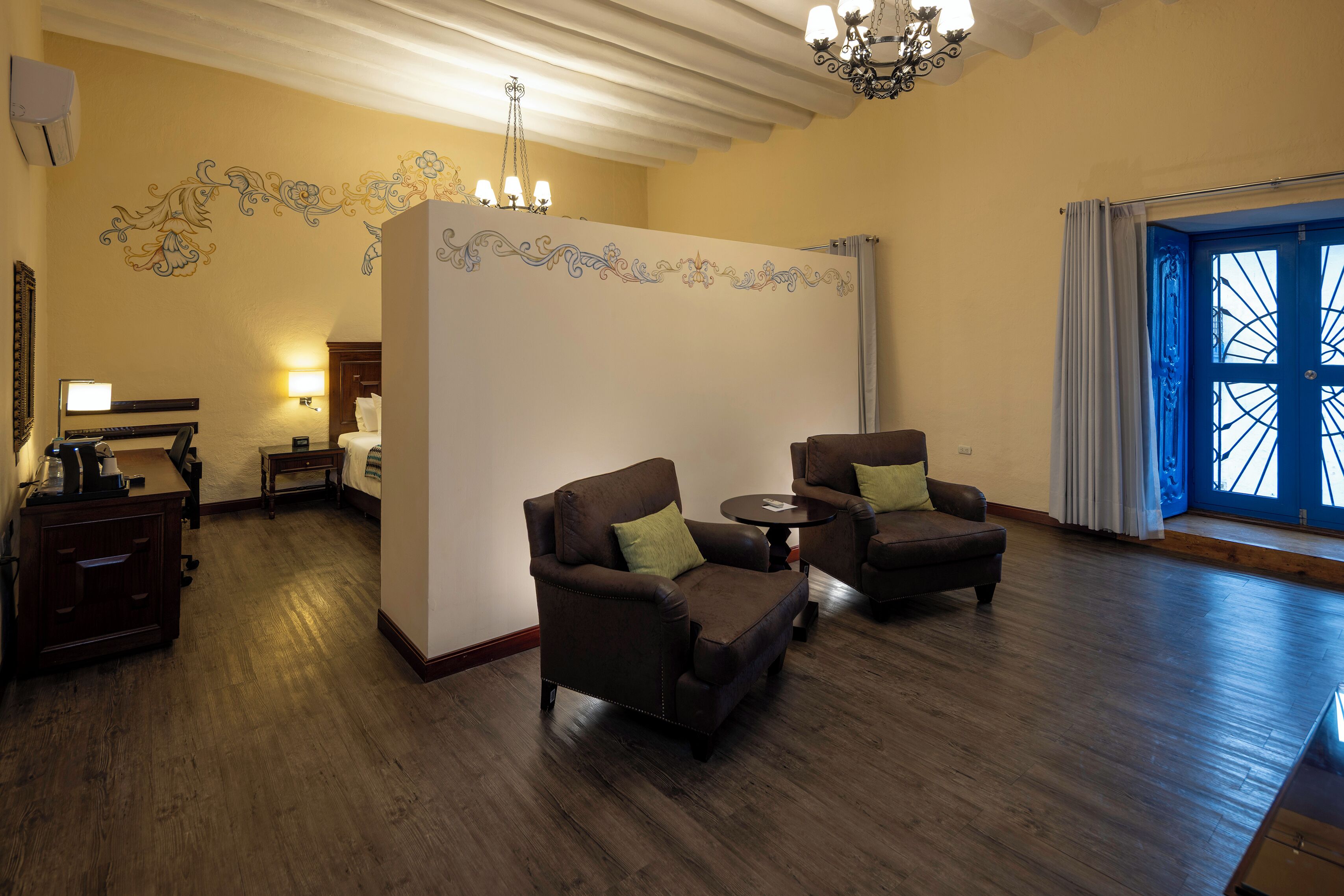 A spacious room with two leather armchairs, a small table, a wooden desk, and a decorative wall with floral patterns.