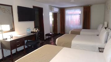 Ett hotellrum med två sängar, ett skrivbord, en stol, en spegel, en tv och ett fönster med gardiner.