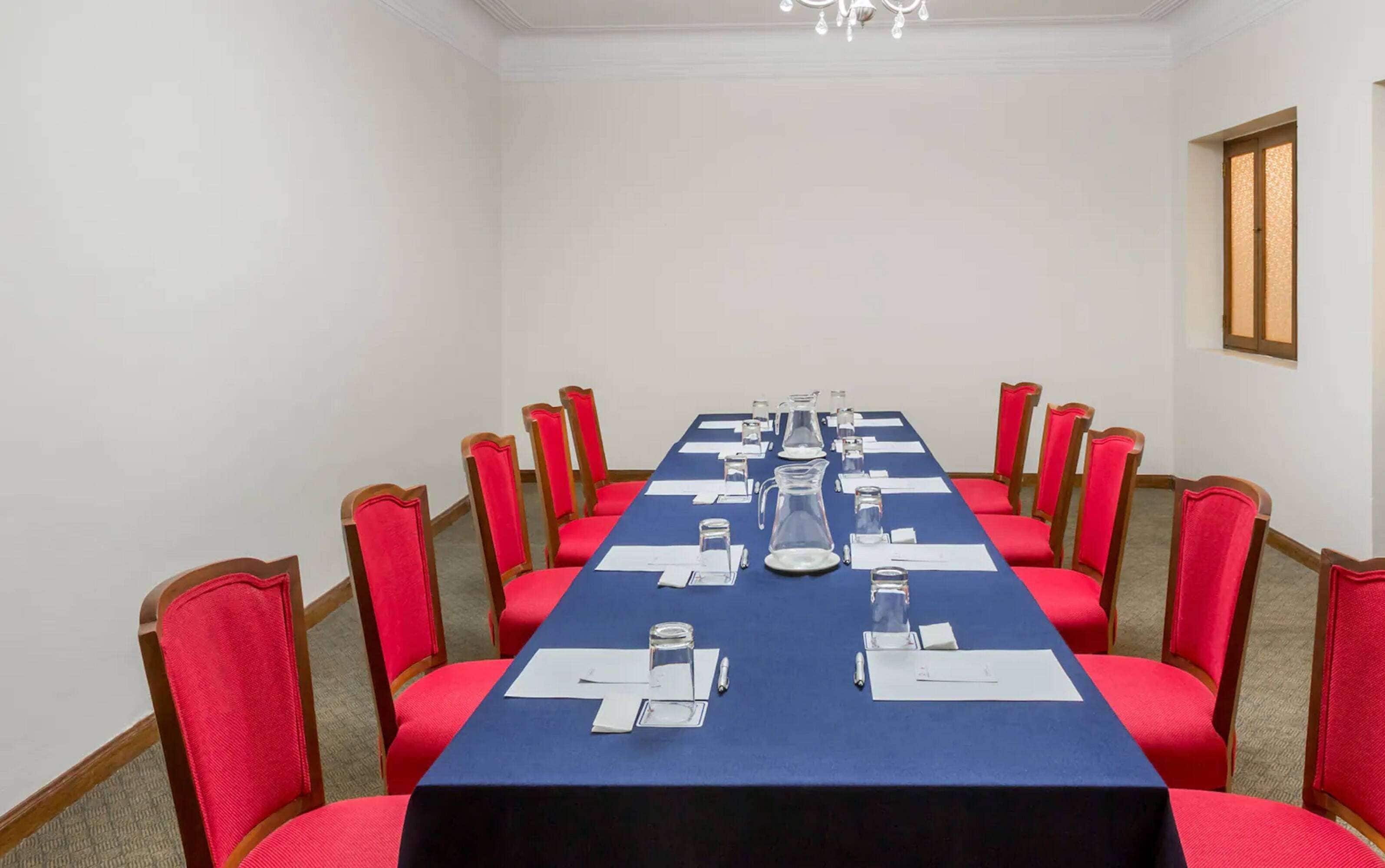 Une salle de conférence avec une longue table, des chaises rouges et un lustre.