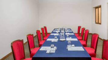 Une salle de conférence avec une longue table, des chaises rouges et un lustre.