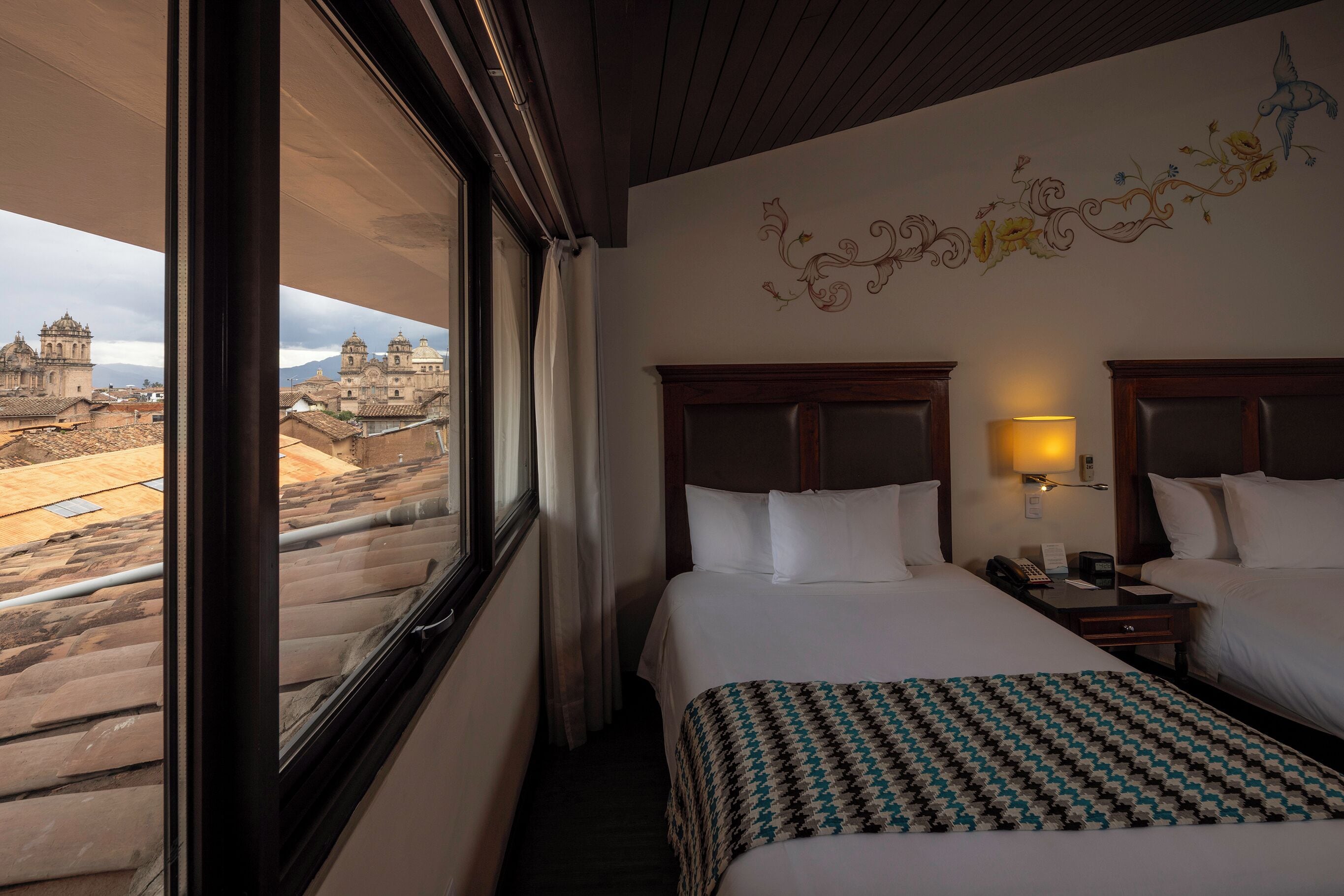 A hotel room with two beds, a view of historic buildings, and a decorative wall mural.
