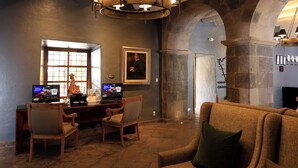 Un vestíbul amb paret de pedra, un taulell de fusta amb dos portàtils, un retrat amb marc i una finestra gran.