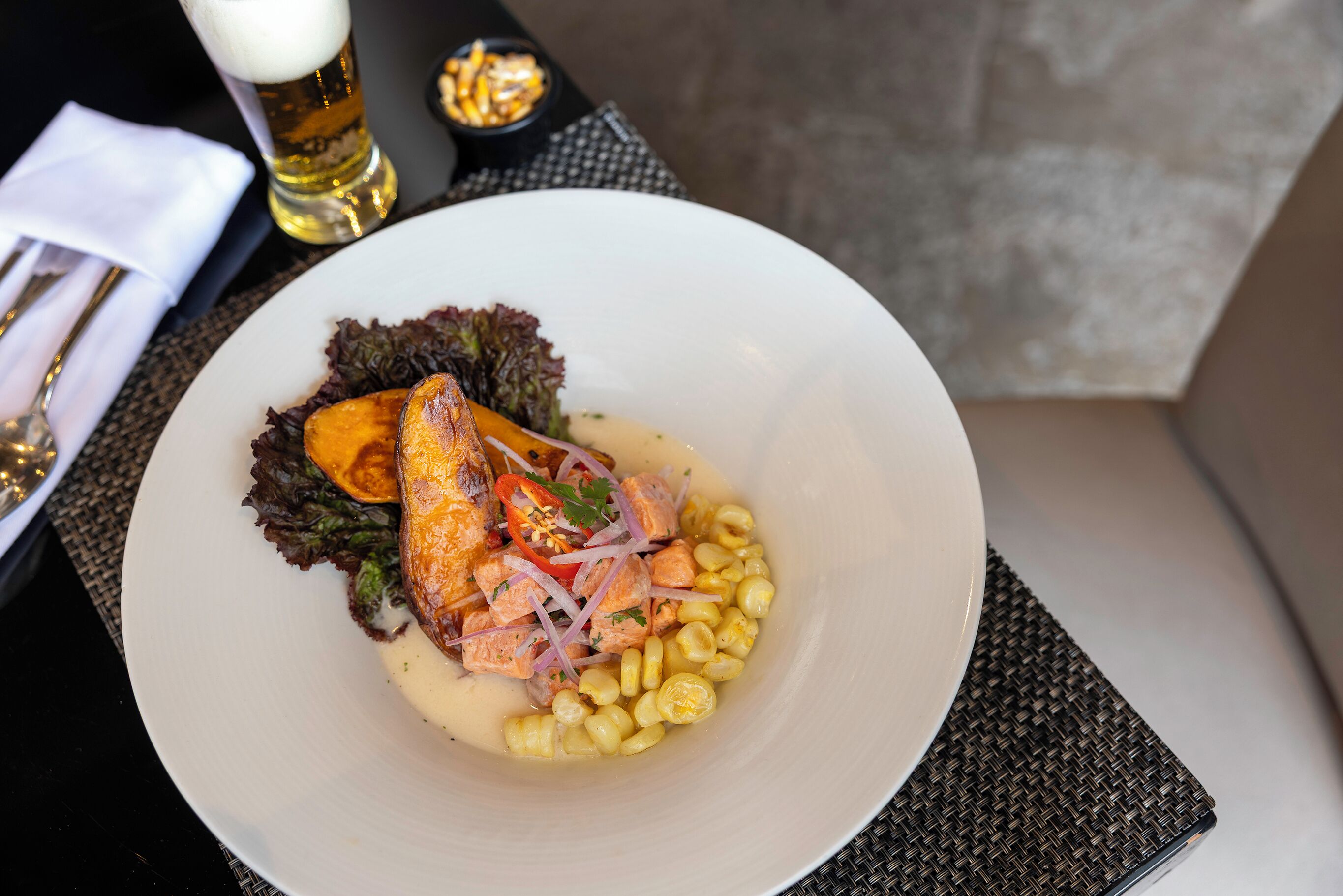 A white plate with salmon, corn, and red onions on a woven placemat.