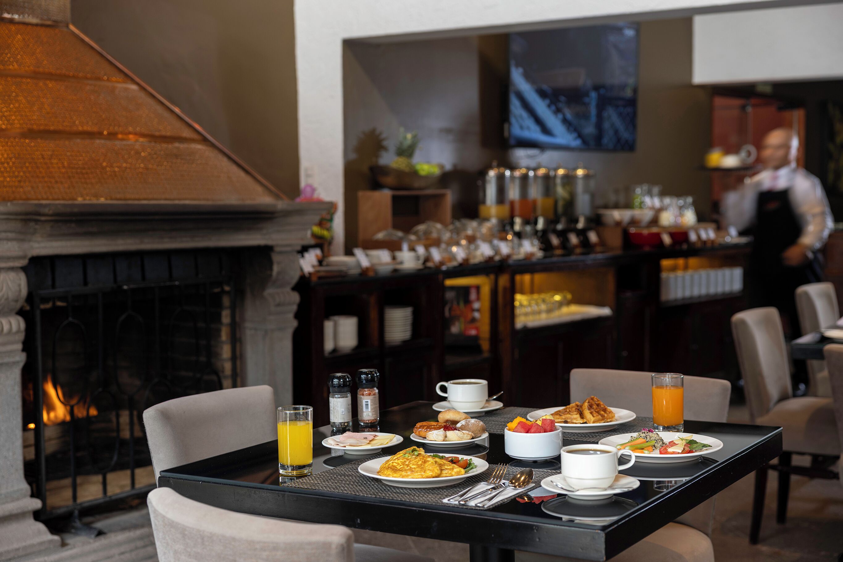 A dining table set with breakfast items, a fireplace, and a bar area with various drinks and condiments.