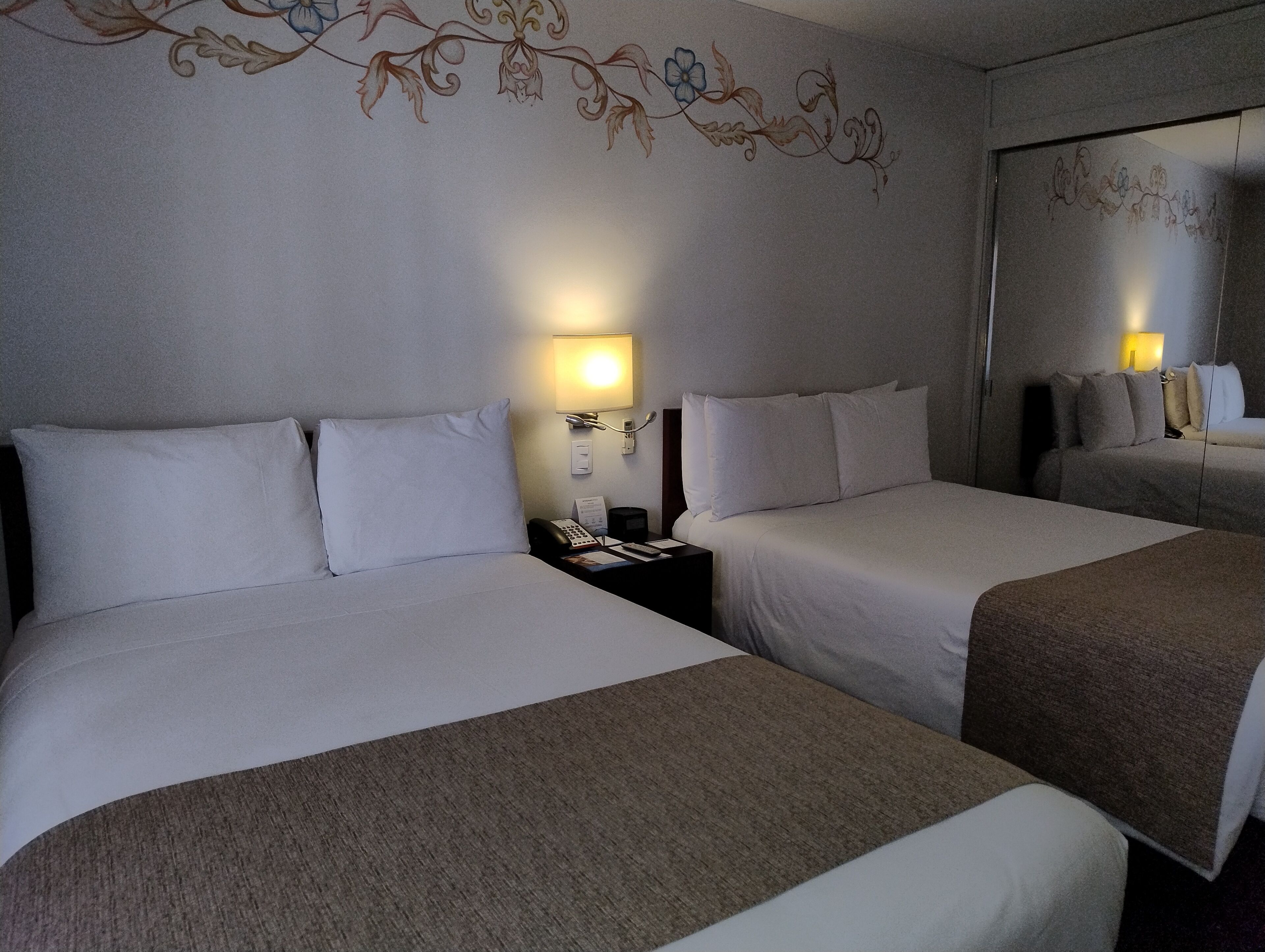 Habitación de hotel con dos camas, una mesita de noche con teléfono y una lámpara de pared.