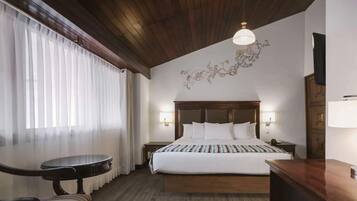 A hotel room with a wooden ceiling, a large bed with white bedding, a small round table, and a chair.