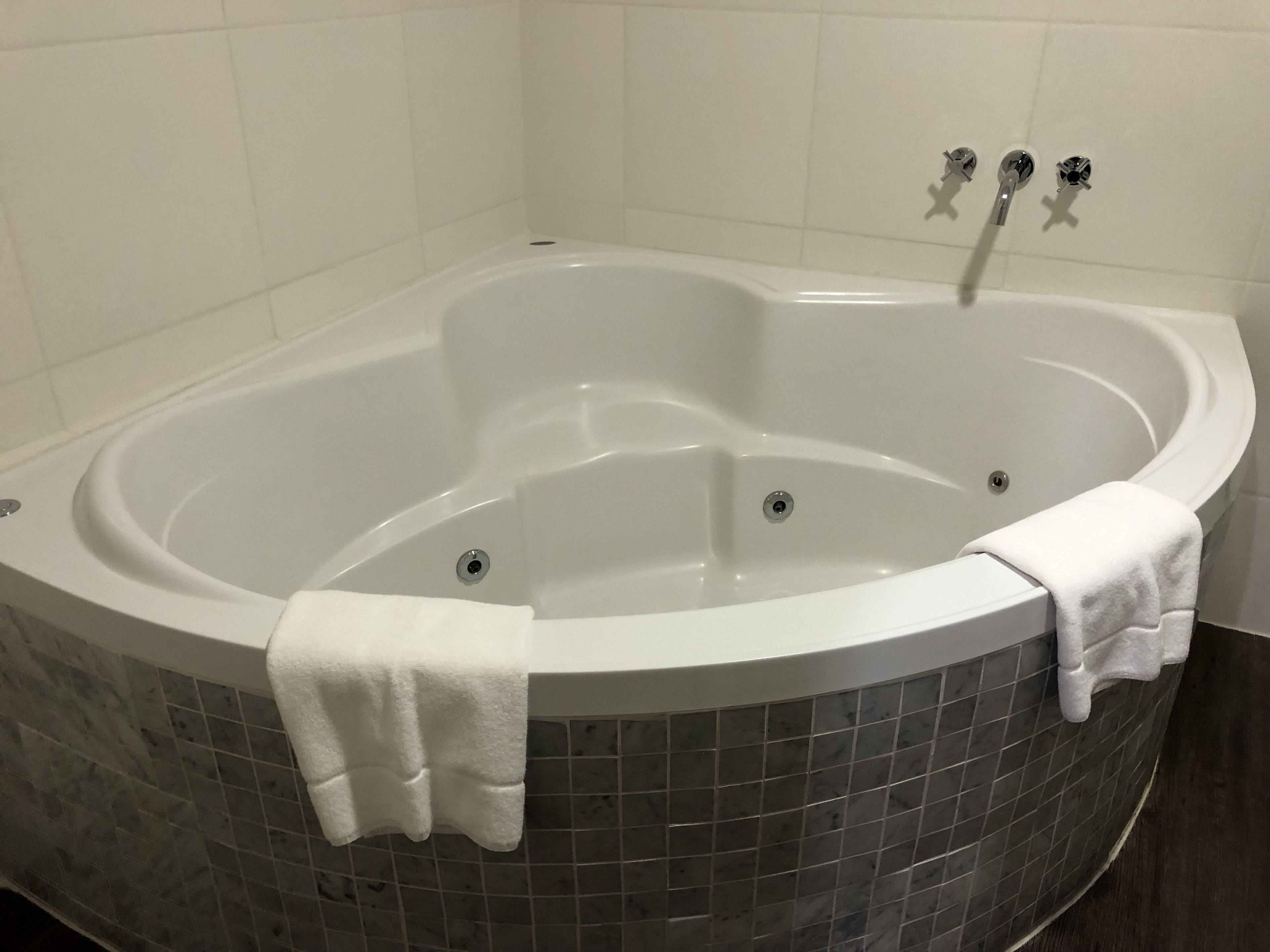A large, freestanding bathtub with a white towel draped over it, set against a tiled wall.