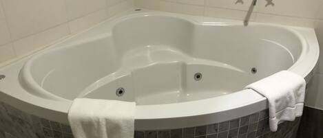 A large, freestanding bathtub with a white towel draped over it, set against a tiled wall.
