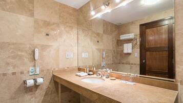 Un baño con pared de mármol color beige, un espejo grande, un lavamanos y una puerta de madera.