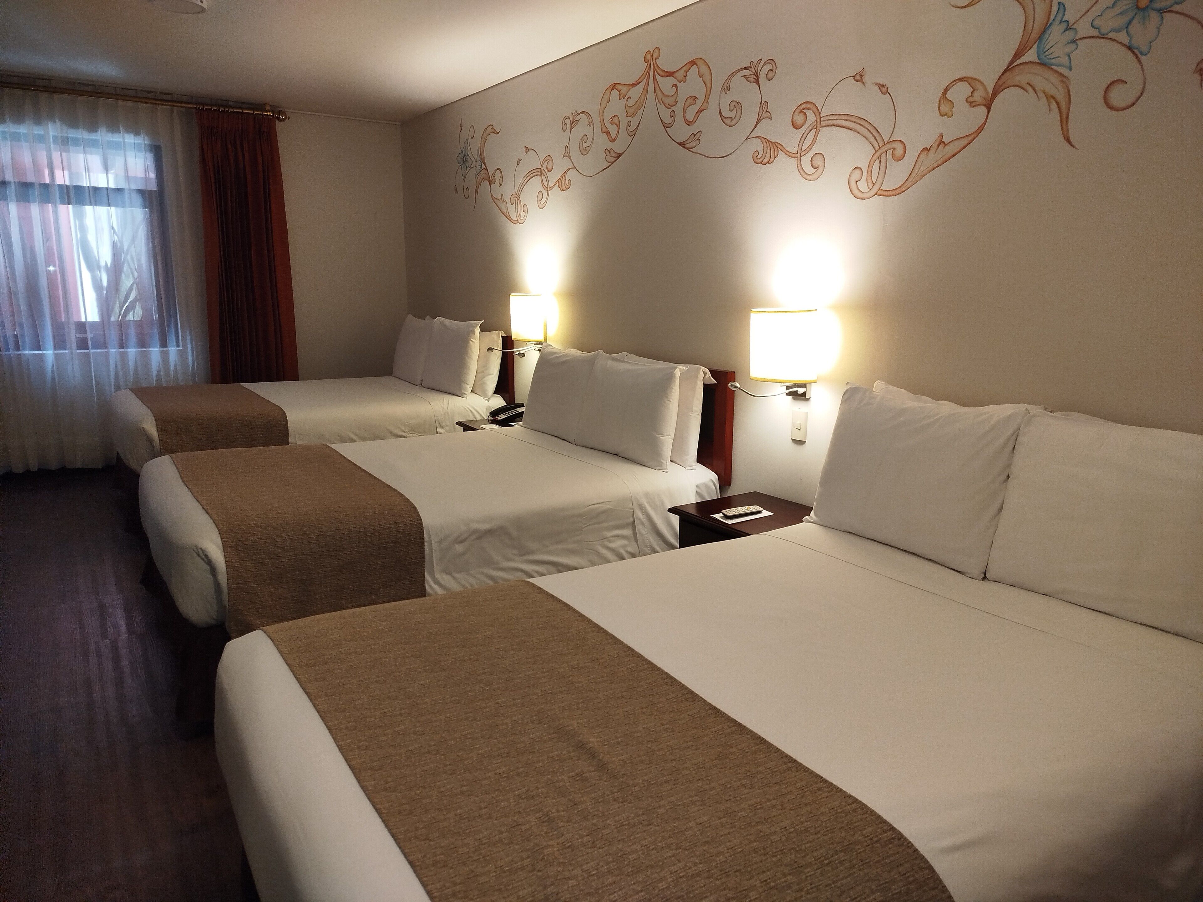 A hotel room with two beds, a bedside table with a lamp, and a decorative wall design.