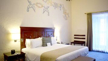 A hotel room with a large bed, bedside tables, a nightstand, a bench, and a window with curtains.