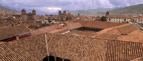 A historic building with a tiled roof and arched windows, surrounded by a cityscape with mountains in the background.