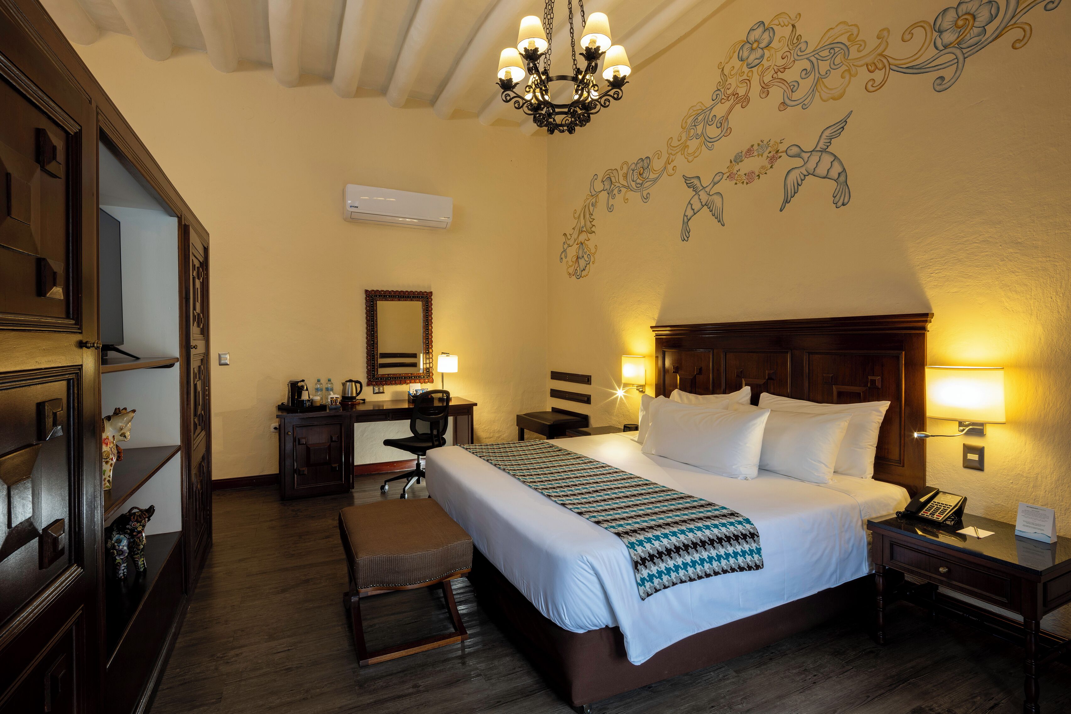 Habitación de hotel con una cama grande, un escritorio, una silla, una mesita y un mural decorativo en la pared.