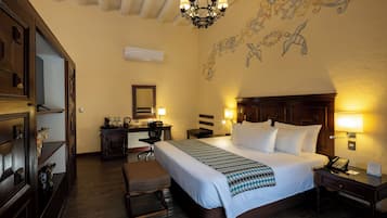 Habitación de hotel con una cama grande, un escritorio, una silla, una mesita y un mural decorativo en la pared.