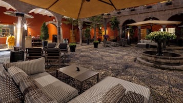 A spacious outdoor seating area with wicker furniture, umbrellas, and potted plants.